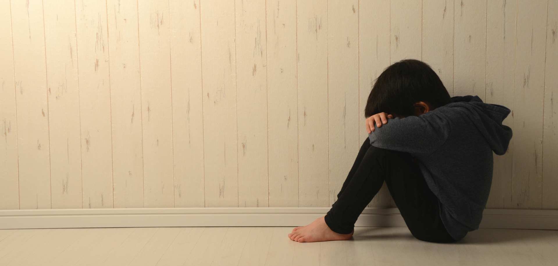 Ein kleiner Junge sitzt mit dem Kopf in den Armen auf dem Boden.