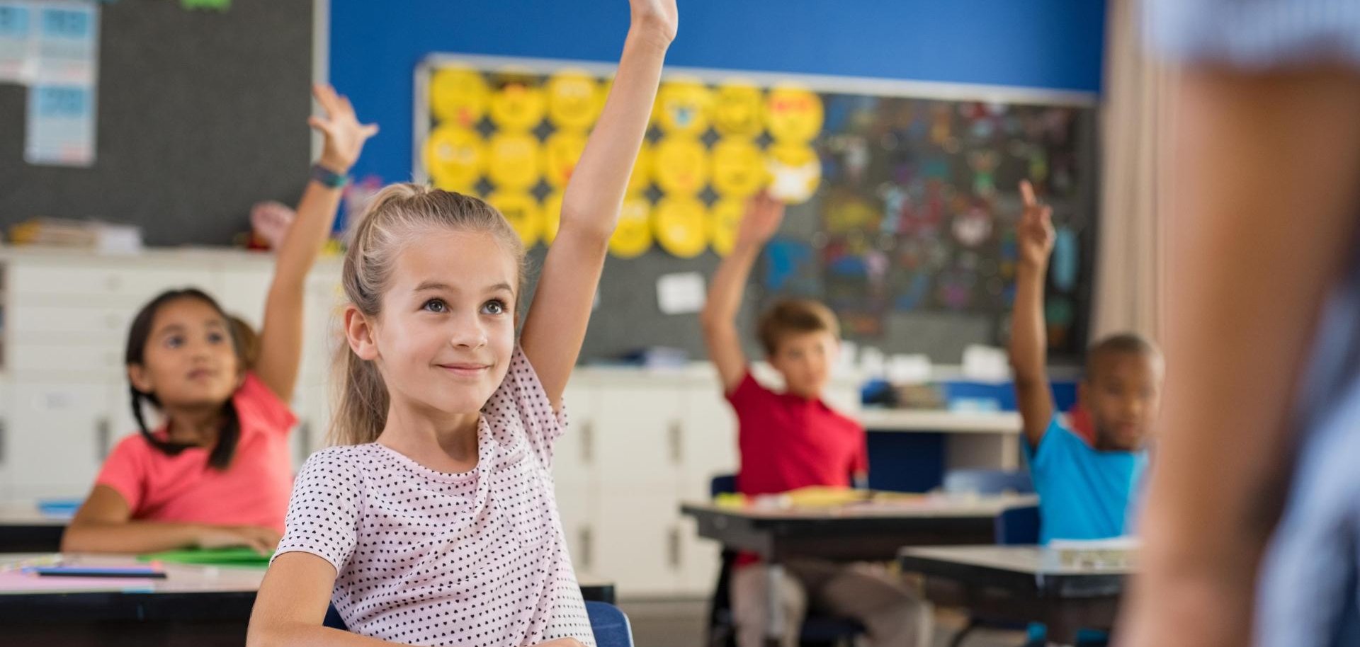 Ein Mädchen sitzt in einem Klassenraum und meldet sich.