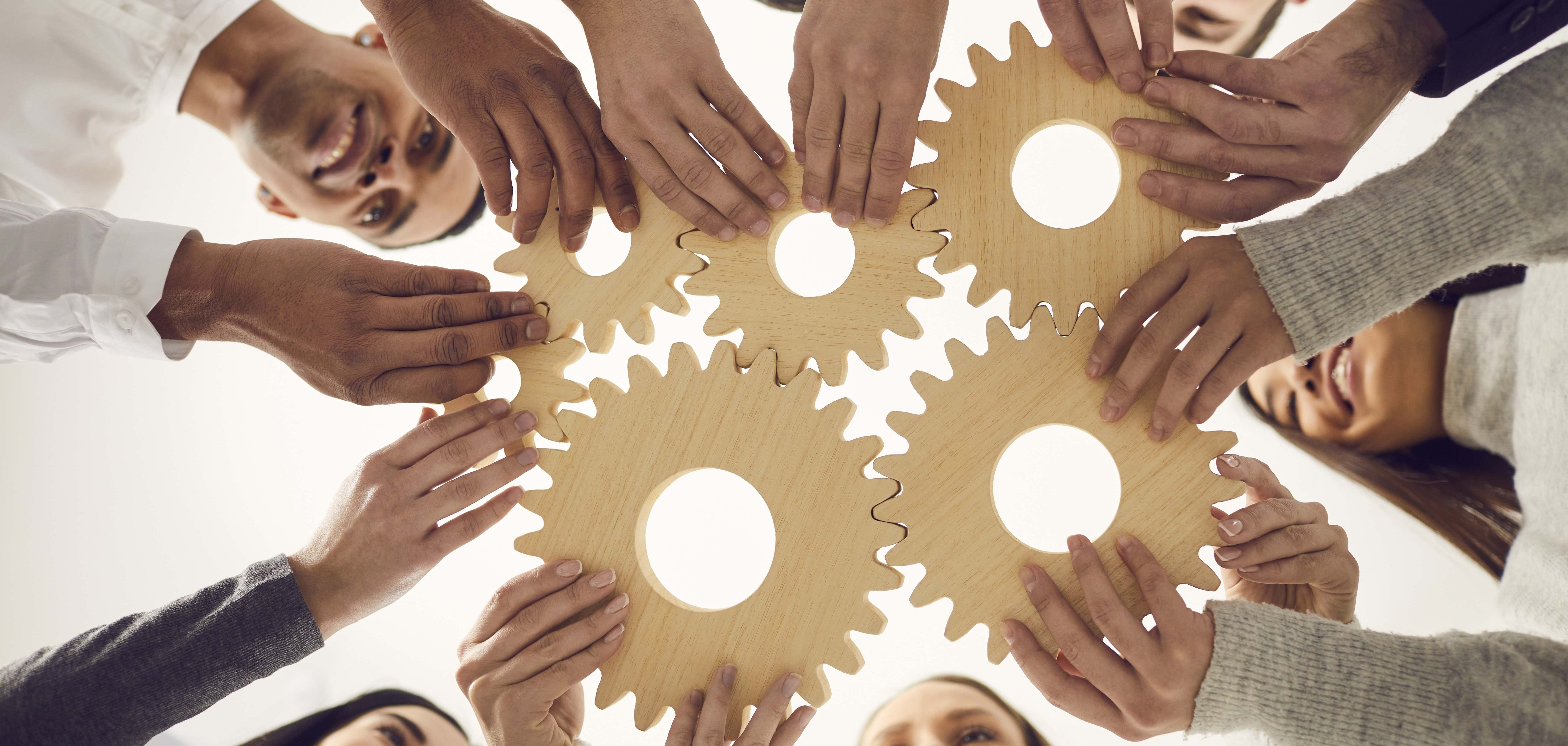 Ein Team von Menschen hält mehrere Zahnräder aneinander.