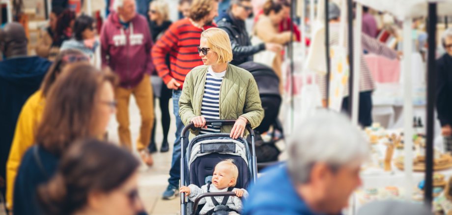 Mother waling and pushing his infant baby boy child in stroller in crowd of unrecognizable people wisiting sunday flea market in Malaga, Spain. Mother waling and pushing his infant baby boy child in stroller in crowd of unrecognizable people wisiting sunday flea market in Malaga, Spain.
