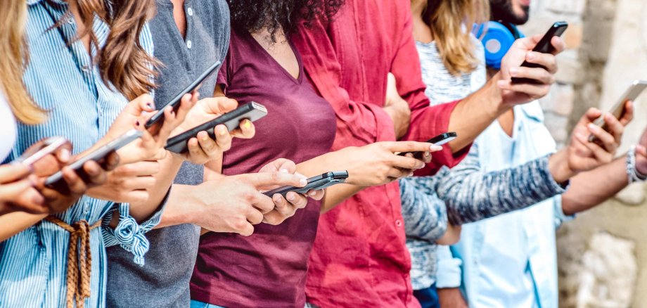 Eine Gruppe junger Menschen steht in einer Reihe und schaut auf Smartphones.