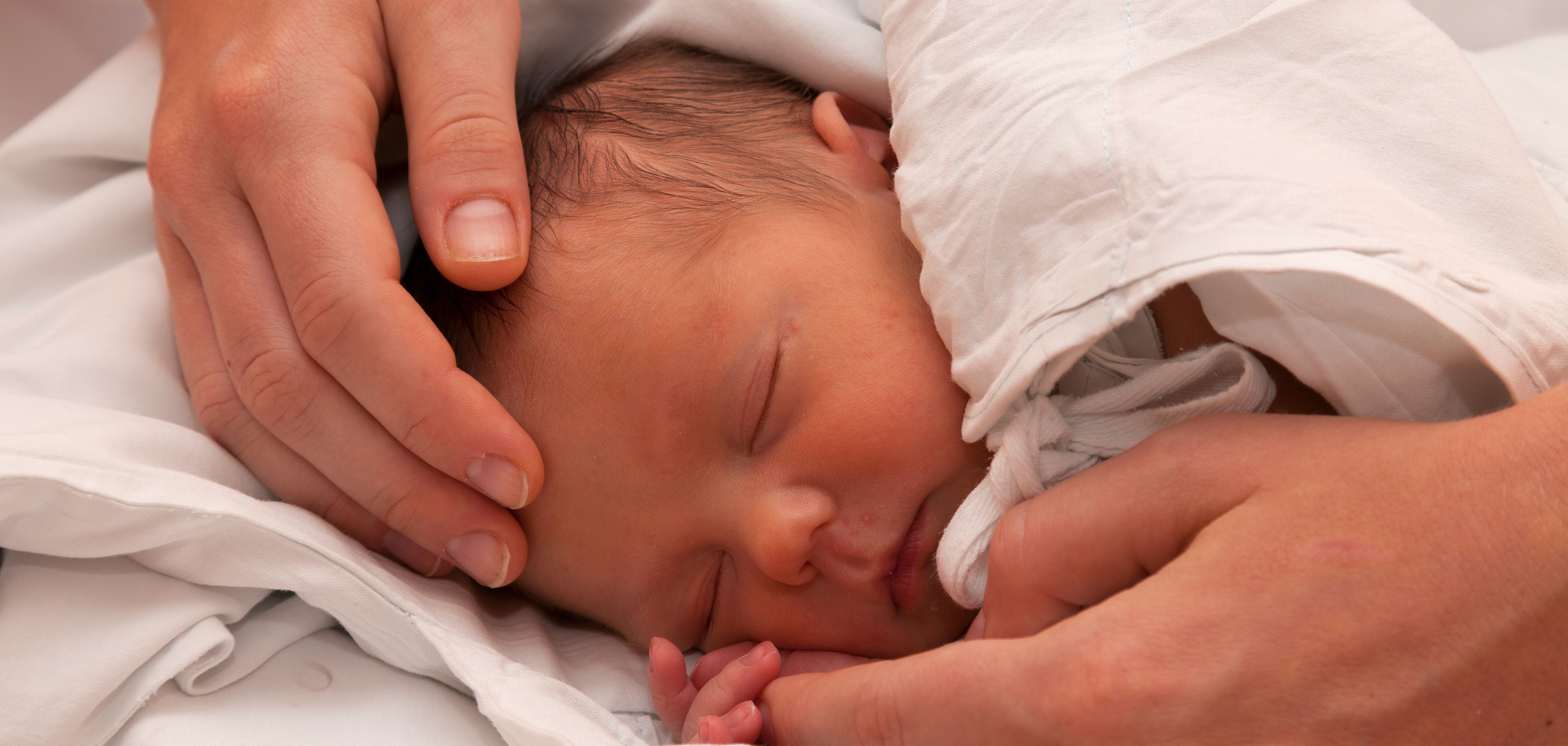 Ein schlafendes neugeborenes Baby hat eine schützende Hand auf dem Kopf.