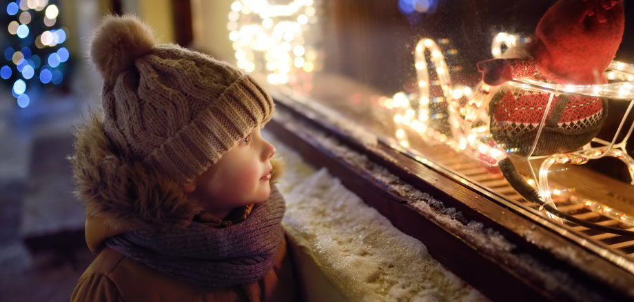 Aktion Weihnachtsfreude Ein kleiner Junge steht vor einem weihnachtlich geschmückten Schaufenster und betrachtet die Lichter.