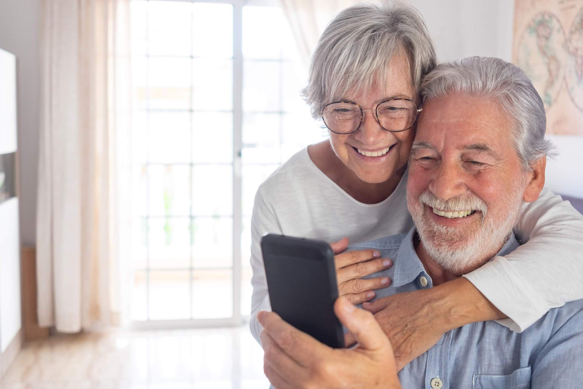 Ein Seniorenpärchen schaut zusammen lächelnd auf ein Handy.