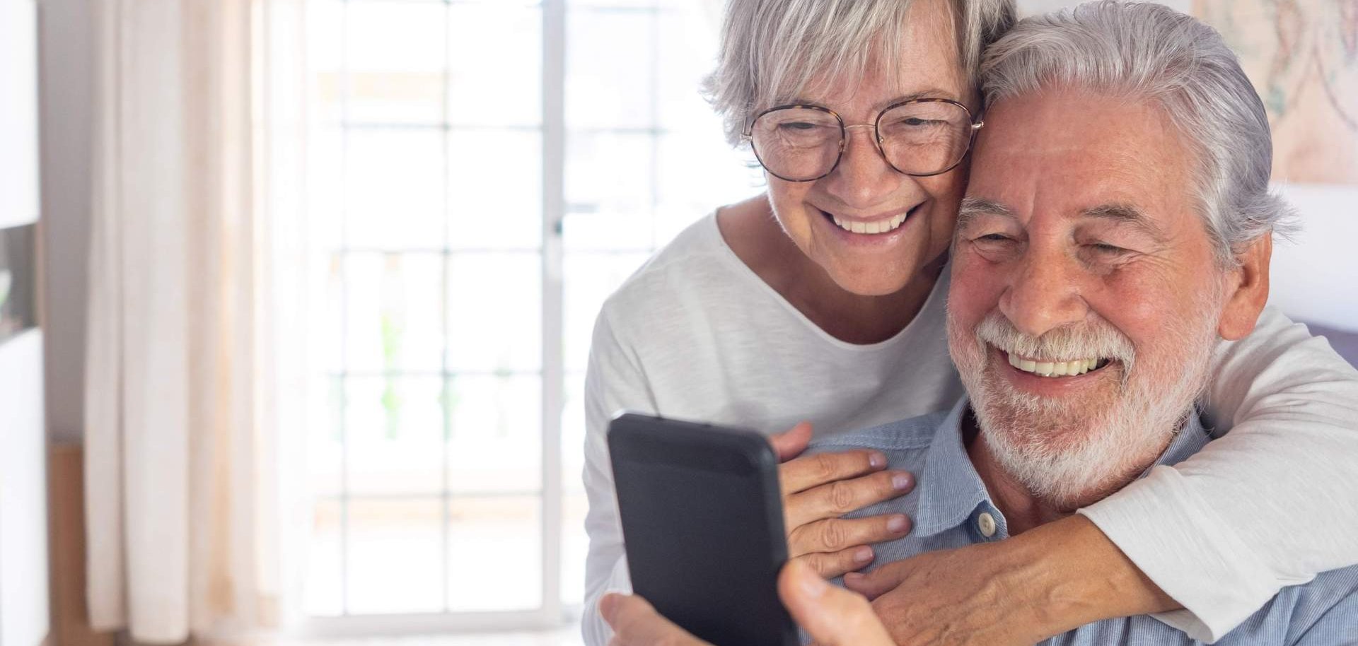 Ein Seniorenpärchen schaut zusammen lächelnd auf ein Handy.
