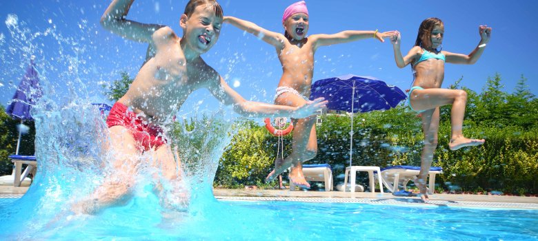 3 Kinder springen vom Beckenrand ins Schwimmbad