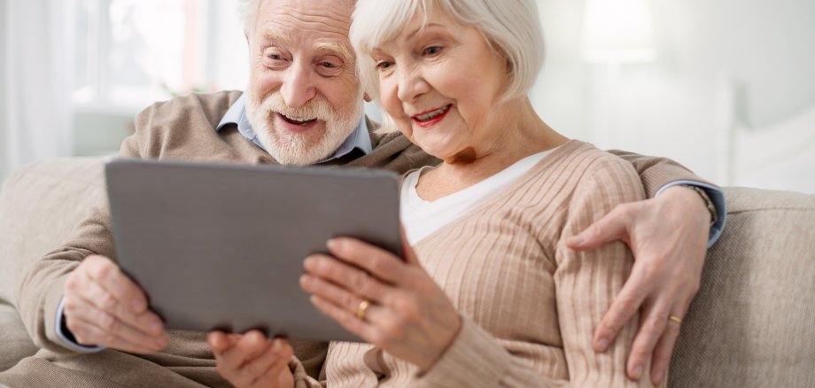 Ein älteres Paar sitzt mit einem Tablet auf dem Sofa.