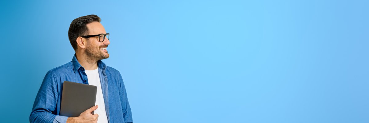 Mann mit Tabelt vor blauem Hintergrund, freut sich, denkt nach Mann, blauer Hintergrund, Brille, Laptop, Freude, Zuversicht, Optimitmus