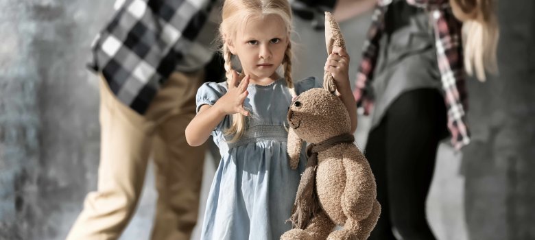 Kleines Mädchen mit Plüsch-Hase. Im Hintergrund streiten die Eltern