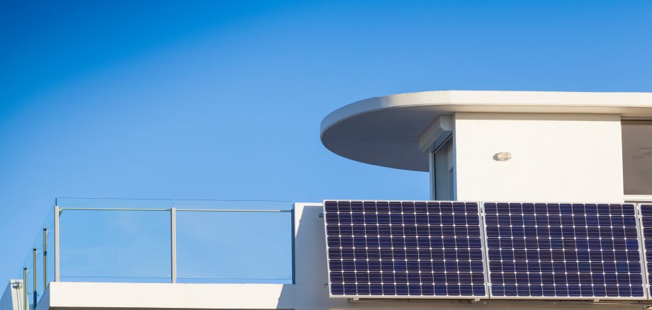 Ein Photovoltaik-Modul ist an einem weißen Hausbalkon angebracht.