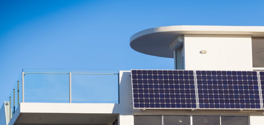 Ein Photovoltaik-Modul ist an einem weißen Hausbalkon angebracht.