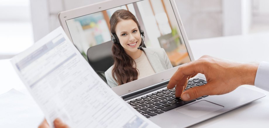 Ein digitales Bewerbungsgespräch, auf dem Laptopbildschirm ist eine junge dunkelhaarige Frau mit Headset zu sehen