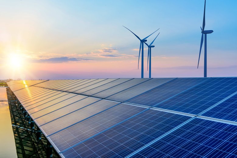 Erneuerbare Energie bei tief stehender Sonnee steht im Vordergrund ist eine Photovoltaikanlage und dahinter drei Windräder.