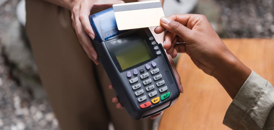 Cropped view of waitress holding payment terminal near african american client with credit card on cafe terrace