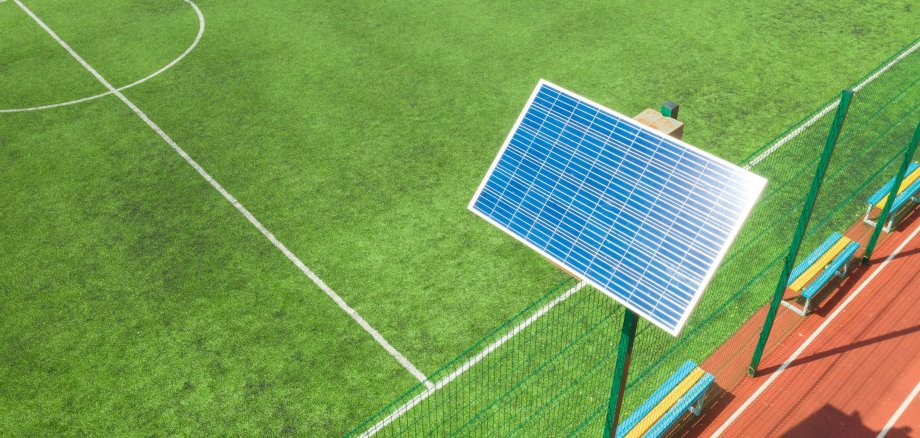 Eine Solaranlage steht direkt an einem  Fußballplatz und glänzt in der Sonne.