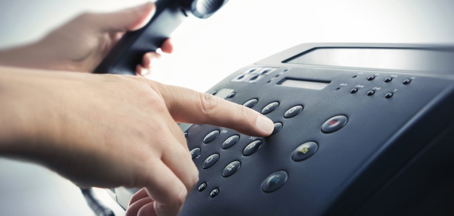 Männliche Hand wählt eine Nummer am Telefon und hat den Hörer in der Hand