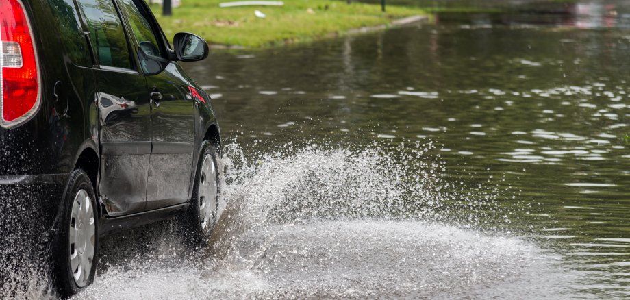 Ein Auto fährt durch eine geflutete Straße.