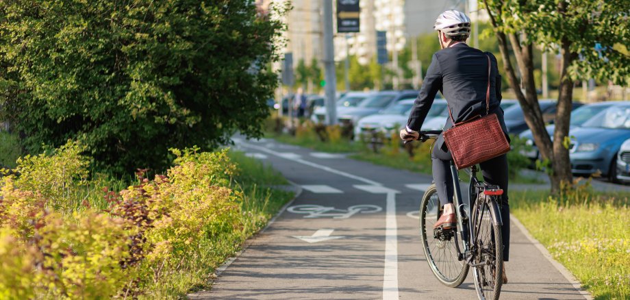 Ein Mann im Anzug steht auf seinem Fahrrad auf einem Fahrradweg in der Stadt.