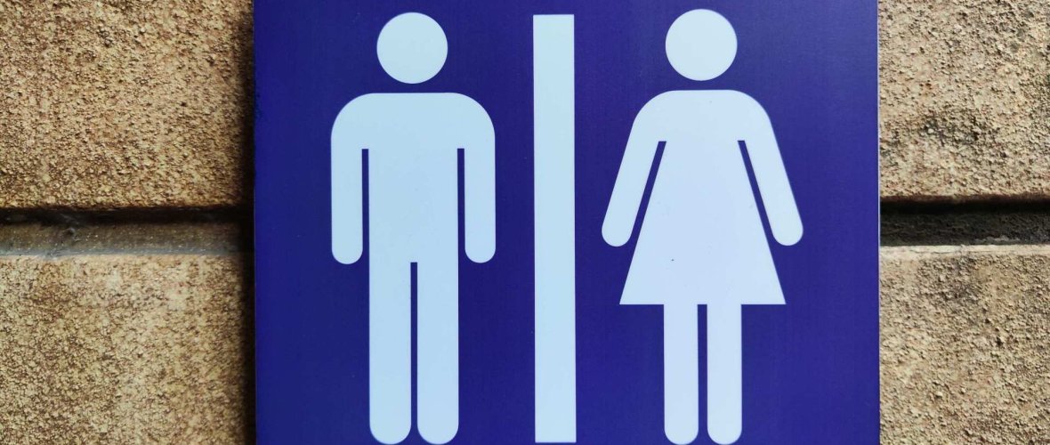 Ein blaues Schild für eine öffentliche Toilette. Zu sehen sind das Symbol für Mann und das Symbol für Frau.