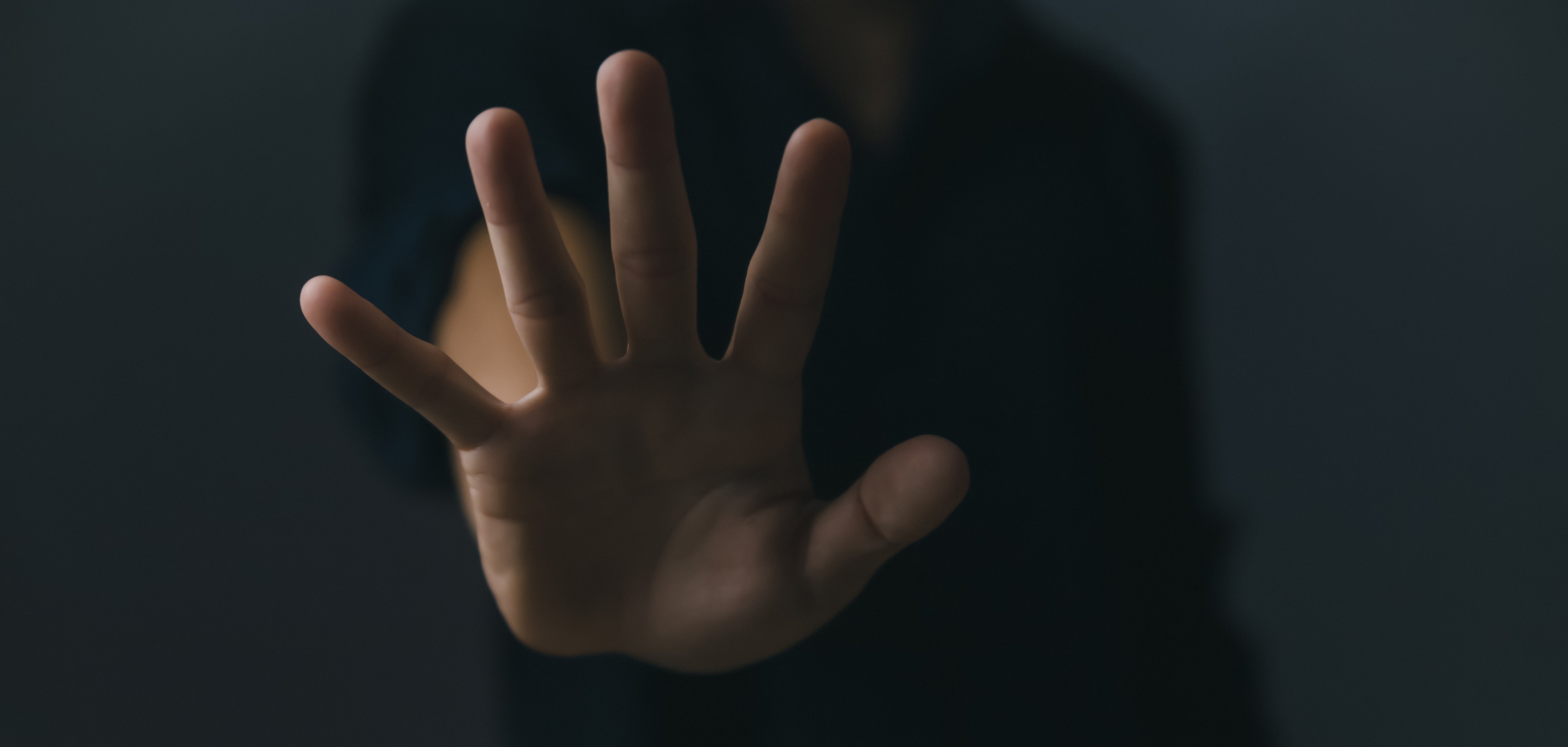 Eine Handfläche in Abwehrhaltung vor dunklem Hintergrund.