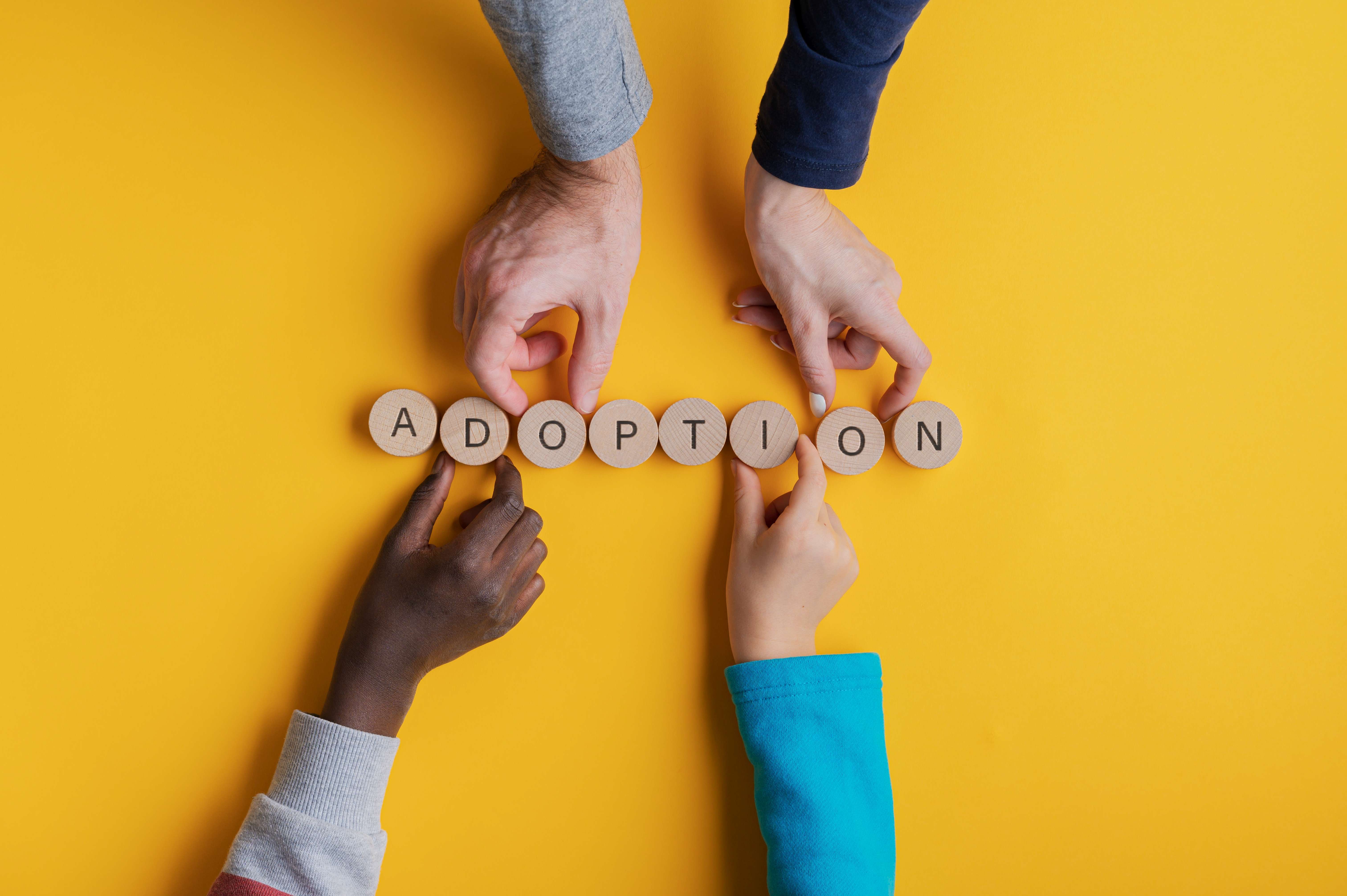 Adoption Vier Hände legen mit Holzbuchstaben das Wort Adoption