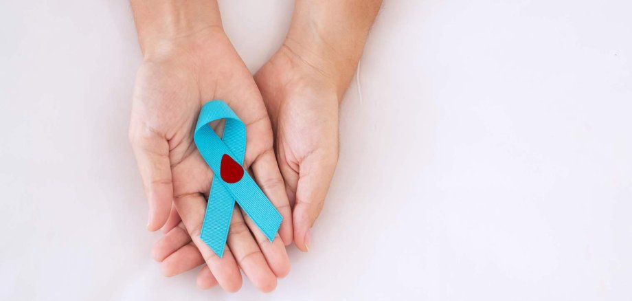 Infoveranstaltung Diabetes Zwei Hände halten eine blaue Schleife, auf der ein Symbol eines Bluttropfens abgebildet ist.