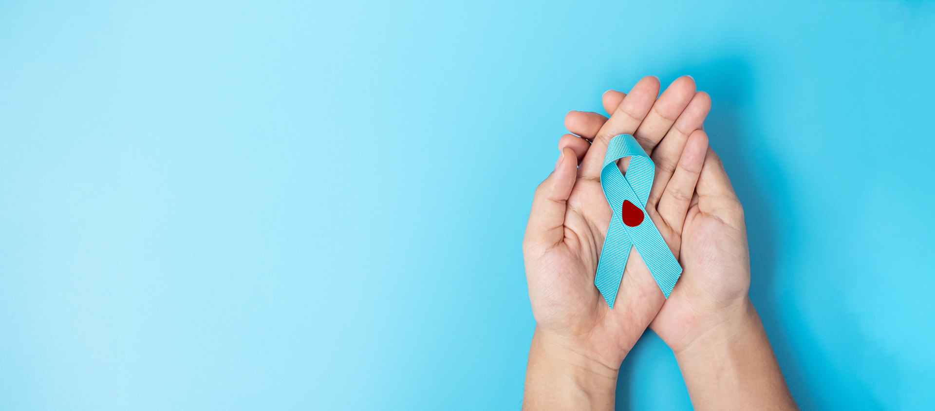 Ein paar Hände halten ein blaues Band mit einem roten Herz darauf.