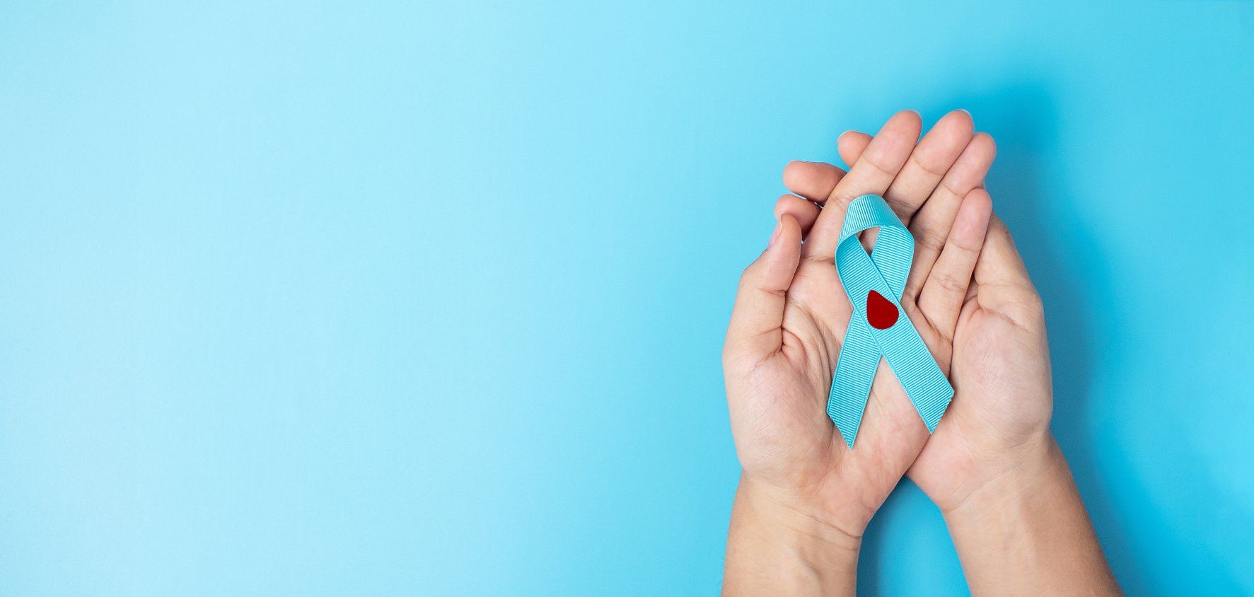 Ein paar Hände halten ein blaues Band mit einem roten Herz darauf.