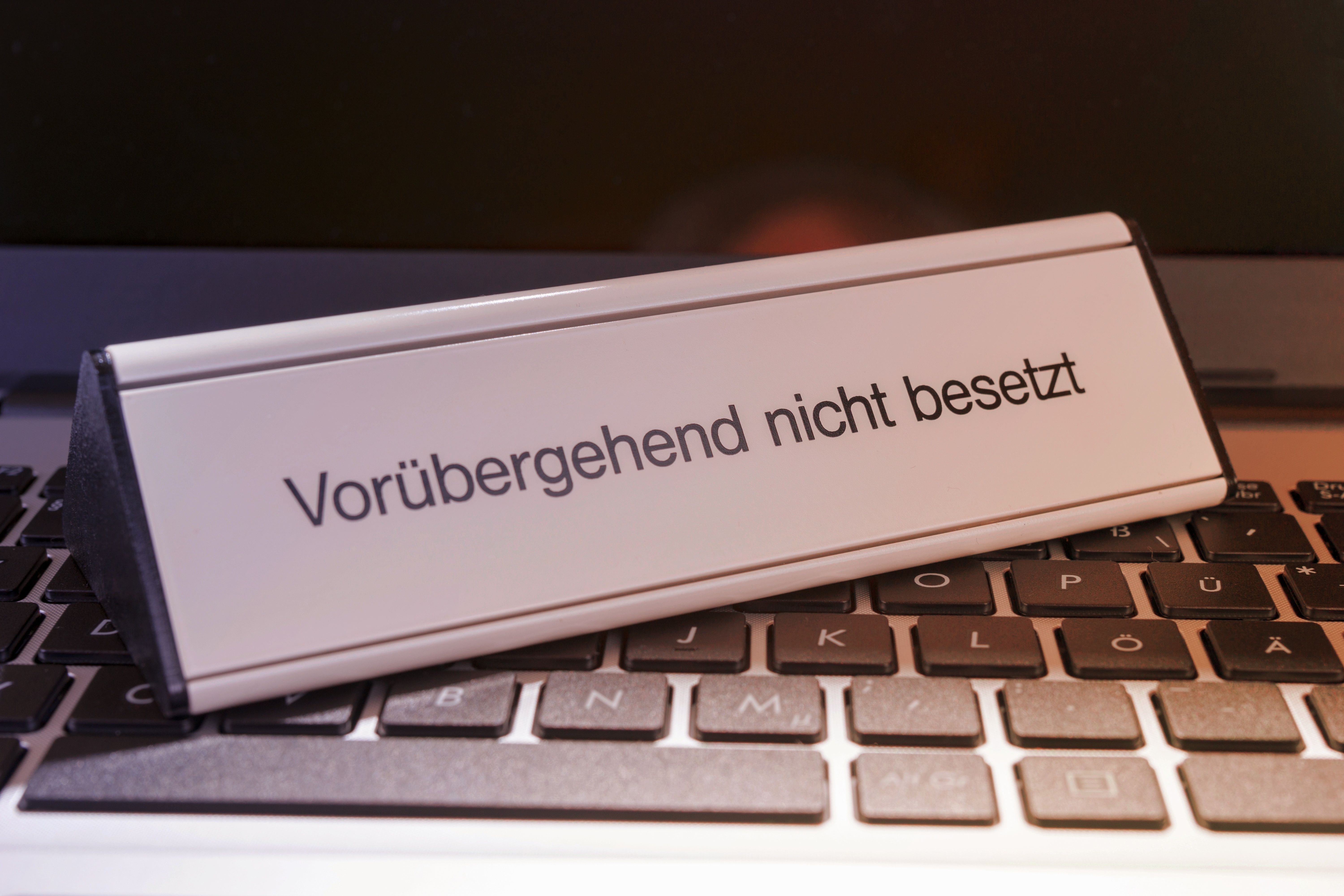 Auf einer schwarzen Tastatur steht ein silbernes Schilt mit der Aufschrift "vorübergehend nicht besetzt"
