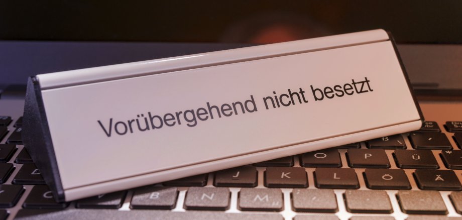 Auf einer schwarzen Tastatur steht ein silbernes Schilt mit der Aufschrift "vorübergehend nicht besetzt"