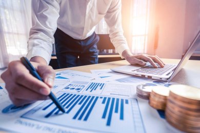 Auswertung eines Graphen mit Hilfe eines Laptops. Unterlagen liegen auf Schreibtisch