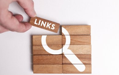 Links Zu sehen sind mehrere Holzstücke, die direkt aneinandergelegt sind und auf denen das Symbol deiner Lupe abgebildet ist. Das Holzstück oben links wird von einer Hand nach oben weggehoben. Auf diesem Baustein steht das Wort Links.