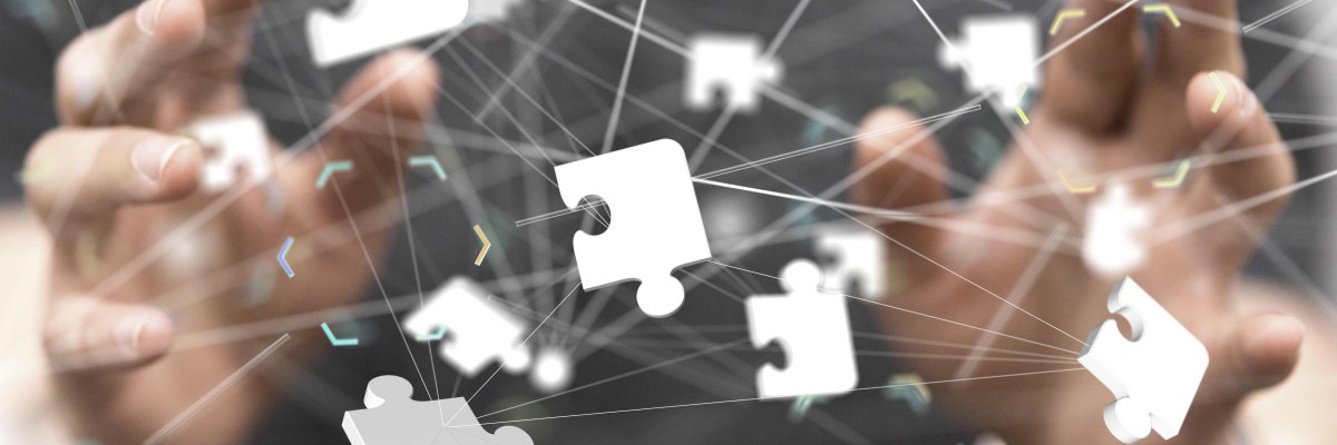 Puzzle Im Vordergrund sind schwebende weiße Puzzelteile zu sehen, im Hintergrund sieht man leicht verschwommen zwei Hände und einen Oberkörper.