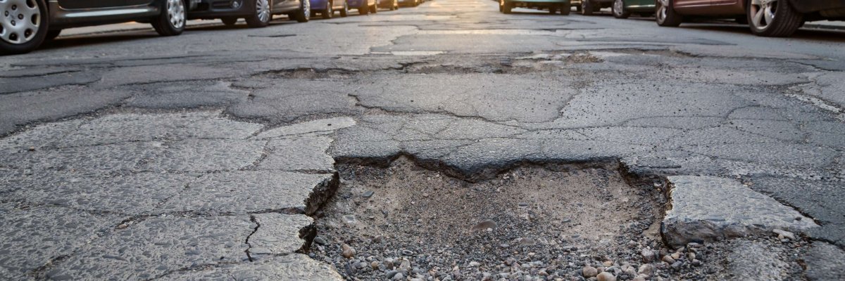 Schlagloch in der Stadt Ein Schlagloch auf einer Straße in der Stadt, rechts uns links parken Autos