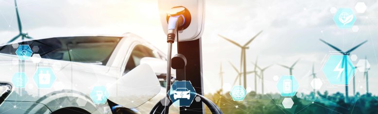 Energie- und Mobilitätswende Ein Auto lädt an einer E-Ladesäule, im Hintergrund sind Windenergieanlagen zu sehen.