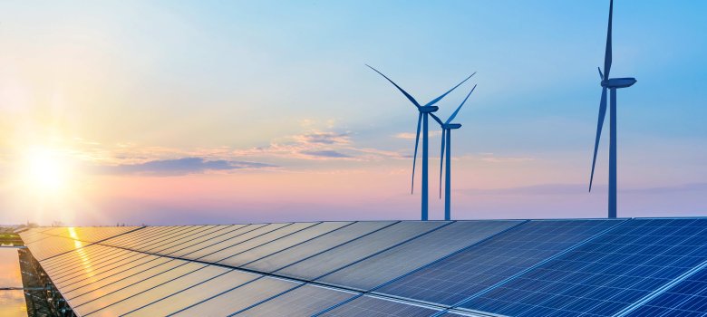bei tief stehender Sonnee steht im Vordergrund ist eine Photovoltaikanlage und dahinter drei Windräder.
