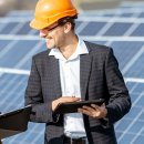 Ein Mann und eine Frau stehen mit Bauhelmen und Tablets vor Photovoltaik-Anlagen