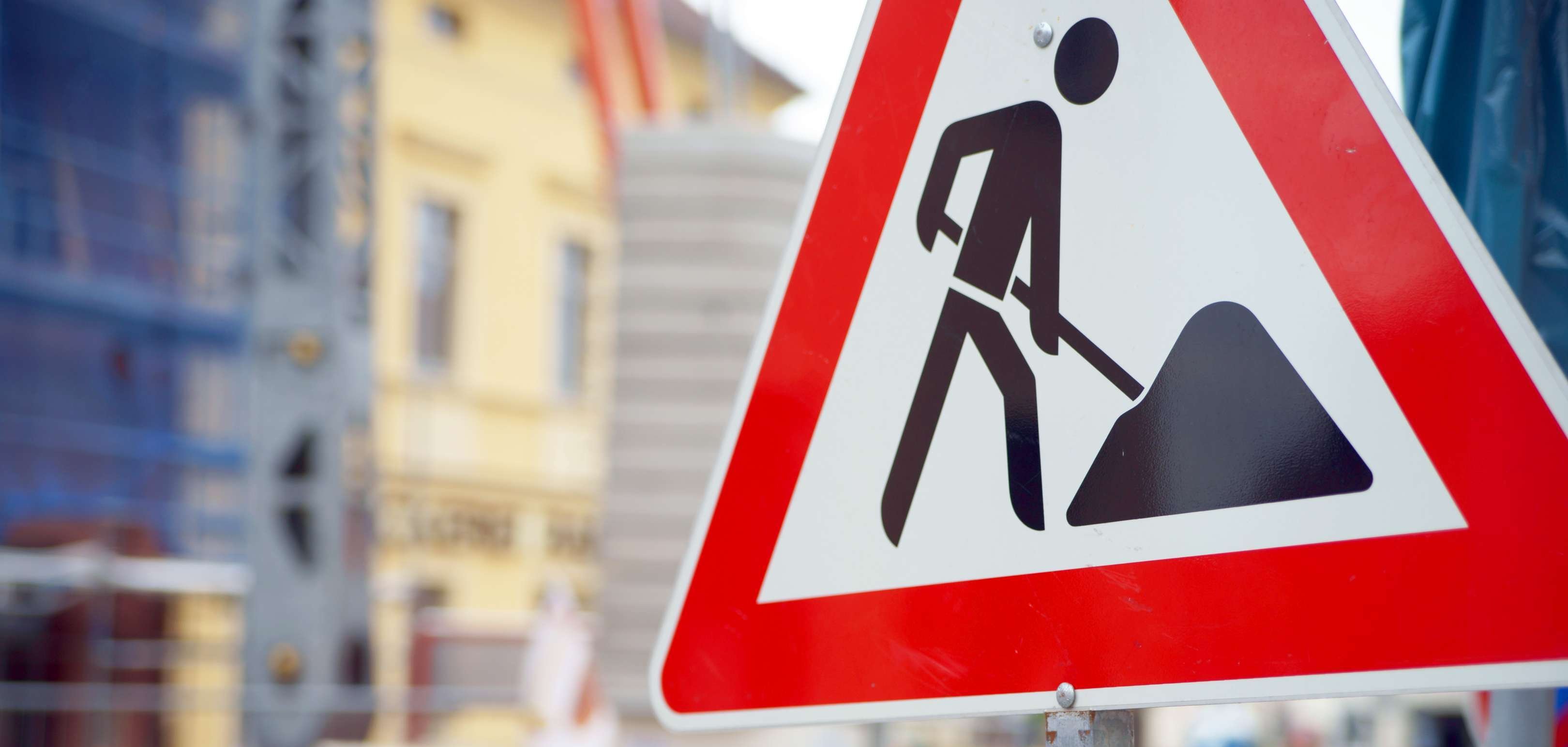 Ein Baustellenschild, im Hintergrund ist verschwommen eine Baustelle zu sehen. 