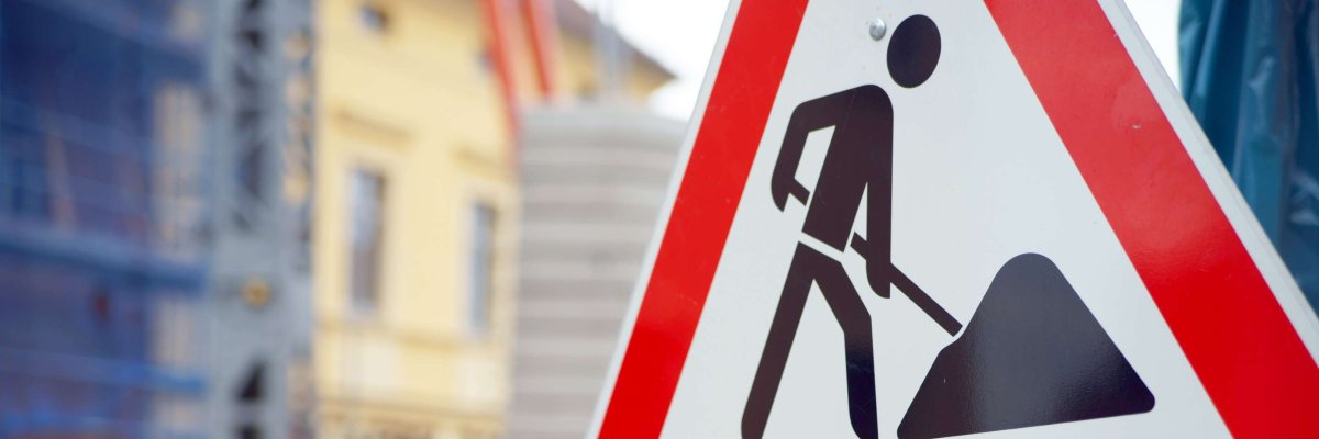 Ein Baustellenschild, im Hintergrund ist verschwommen eine Baustelle zu sehen. 