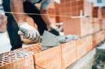 Zu sehen ist ein Bauarbeiter, der eine Mauer baut