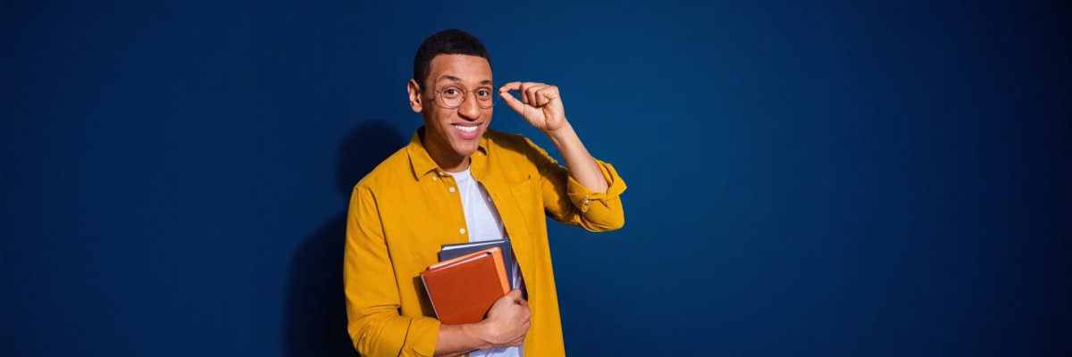Photo of young genius handsome guy in yellow shirt touching his eyeglasses holding books isolated on dark blue color background Photo of young genius handsome guy in yellow shirt touching his eyeglasses holding books isolated on dark blue color background