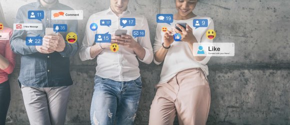 Vier Junge Menschen kontrollieren ihre Sozialenmedien auf ihren Handys an einer Betonwand gelehnt