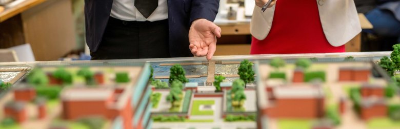 Eine Miniaturnachbildung einer Innenstadt hinter der ein Mann und eine Frau in Business-Kleidung stehen und auf das Modell zeigen.
