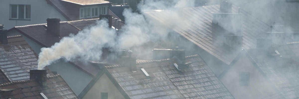 Man sieht die Dächer mehrerer Häuser an einem grauen Wintertag. Aus den Schornsteinen zieht grauer Rauch vom Heizen.